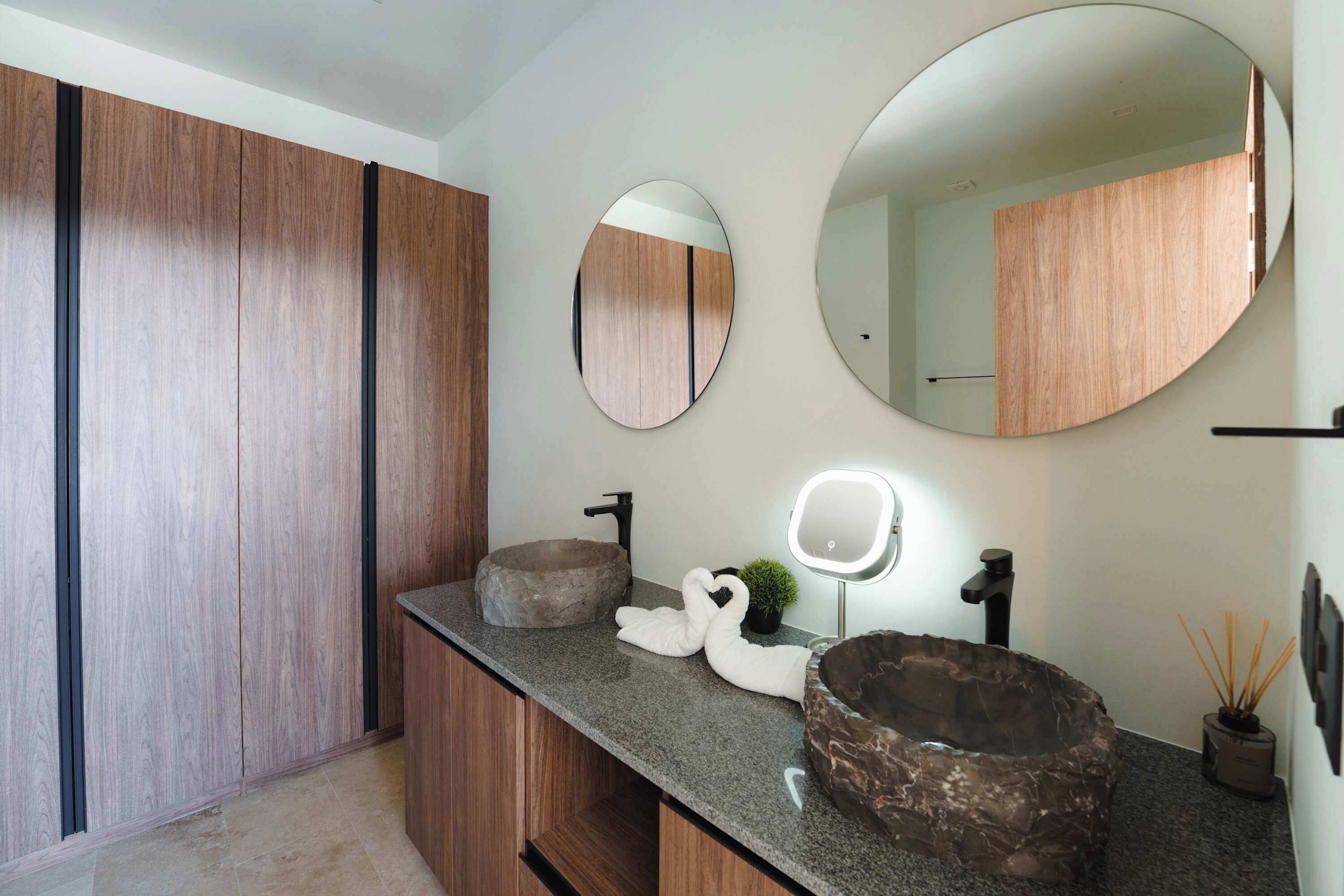 A bathroom with a wooden vanity, two round mirrors, a stone sink, and a decorative swan.
