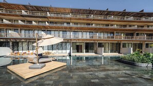 Een meerlaags hotel met een zwembad op het dak, met ligbedden, een houten terras en een grote parasol.
