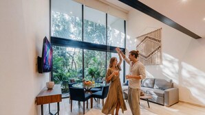 A modern living room with a large window, a round dining table, and a sofa. - Luxury Two-Level Loft in Tulum with Pool & Gym (Tulum)