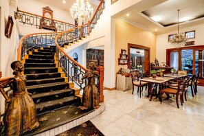 A grand staircase with ornate railings, a chandelier, and a dining area with wooden furniture. - Luxury Deluxe DBL Retreat W/ Free WiFi and Parking (Bandung)