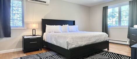A bedroom with a bed, bedside table, lamp, air conditioning unit, and a patterned rug.