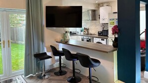 Una cucina moderna con una TV a schermo piatto, un angolo bar con sgabelli e una porta scorrevole in vetro verso un giardino.