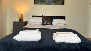 Camera d'albergo con un letto, cuscini, un comodino con una lampada e un'opera d'arte a tema pavone.