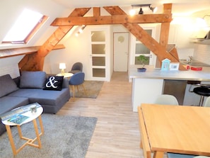 Un espace de vie de style « loft », avec un plafond en pente, un coin repas, une cuisine et un espace détente comprenant un canapé et des fauteuils.