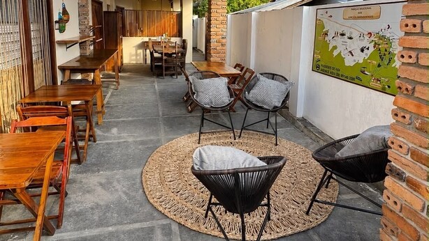 An outdoor covered patio with wooden tables and chairs, a woven rug, and a brick wall with a map. - Urra Village Pousada Atins (Atins)