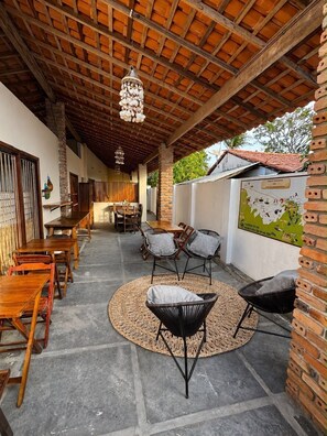 An outdoor covered patio with wooden tables and chairs, a woven rug, and a brick wall with a map.