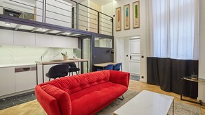 Een modern appartement met een rode bank, een eethoek, een keuken en een trap naar een entresol.