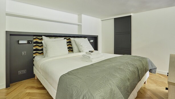 Een moderne slaapkamer met een groot bed, een grijze hoofdeinde en een grijze deur.