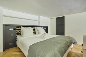 A modern bedroom with a large bed, a grey headboard, and a grey door. - Duplex Center of Paris (Paris)
