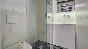 Een moderne badkamer met een douchecabine van glas, een witte wastafel en een betegelde wand van marmer.