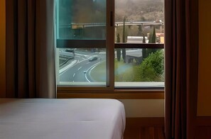 A hotel room with a bed, a window with a view of a road and greenery. - HOTEL EIBAR (Eibar)
