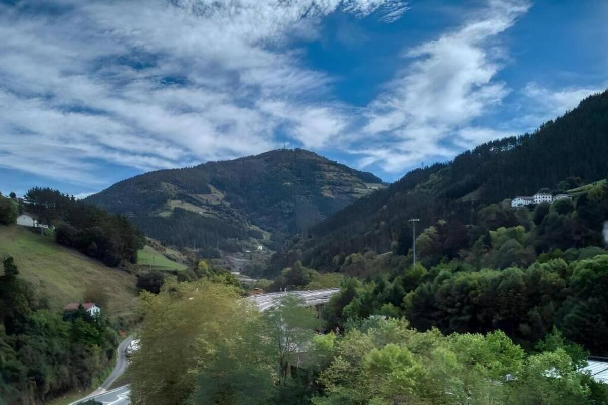 Un valle con una carretera, una montaña y un edificio a lo lejos.