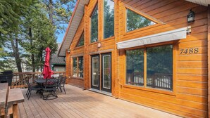 A wooden cabin with a deck, a dining area with outdoor furniture, and a large window with the number 7488.