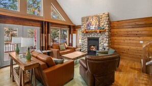 A spacious living room with a stone fireplace, leather furniture, and large windows.
