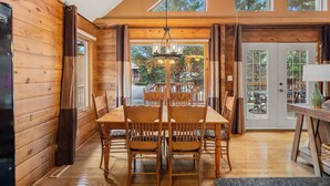 A wooden interior with a dining table and chairs, large windows, and a view of the outdoors.