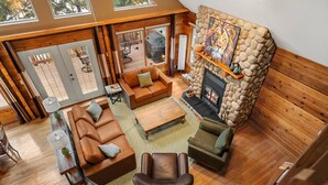 A spacious living area with a stone fireplace, leather sofas, and a view of the outdoors.