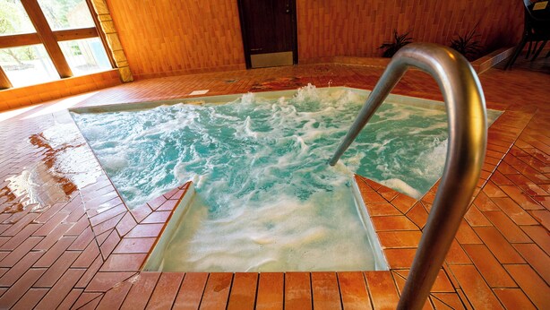A hot tub with a metal faucet, surrounded by tiled flooring and wooden walls. - Pere Marquette Lodge and Conference  (Grafton)