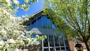 A building with large windows, a stone wall, and a tree with white flowers. - Pere Marquette Lodge and Conference  (Grafton)