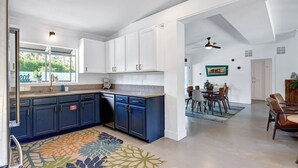 Una cocina moderna con armarios blancos y azules, una zona de comedor con mesa y sillas, y un ventilador de techo.