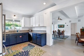 Eine moderne Küche mit weißen und blauen Schränken, ein Essbereich mit Tisch und Stühlen sowie ein Deckenventilator.