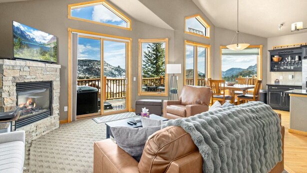 A spacious living room with a stone fireplace, leather sofa, and a dining area with a view of mountains. - Estes Park retreat w/ hot tub, fireplace, king suite (Estes Park)