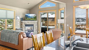 A cozy living room with a fireplace, a sofa, and a dining area with a view of mountains. - Estes Park retreat w/ hot tub, fireplace, king suite (Estes Park)