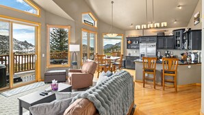 A spacious living area with a sofa, chairs, a coffee table, and a view of a deck. - Estes Park retreat w/ hot tub, fireplace, king suite (Estes Park)