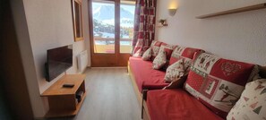 Ein gemütliches Wohnzimmer mit einer Couch, einem Fernseher und Blick auf einen verschneiten Berg.