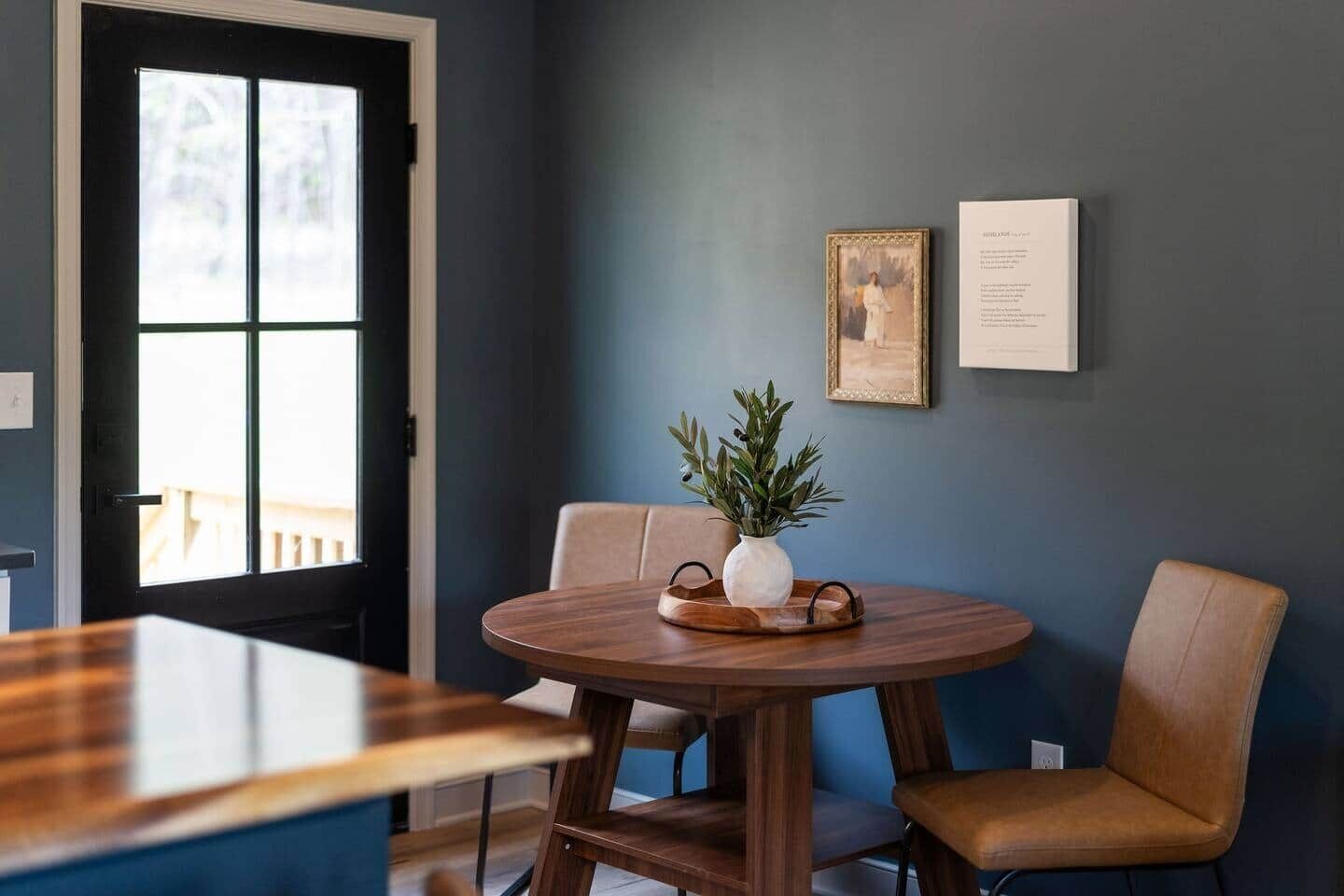 Un coin repas avec une table ronde en bois, deux chaises, un vase avec des plantes et des tableaux encadrés au mur.