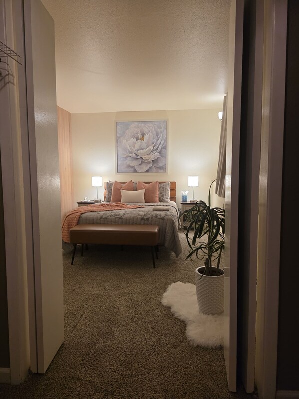 Quarto com cama, abajures, uma grande obra de arte floral, um banco e um vaso com planta.