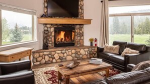 Ein Wohnzimmer mit Kamin aus Stein, Ledersofas, einem Couchtisch und einem Fernseher, der über dem Kamin angebracht ist.