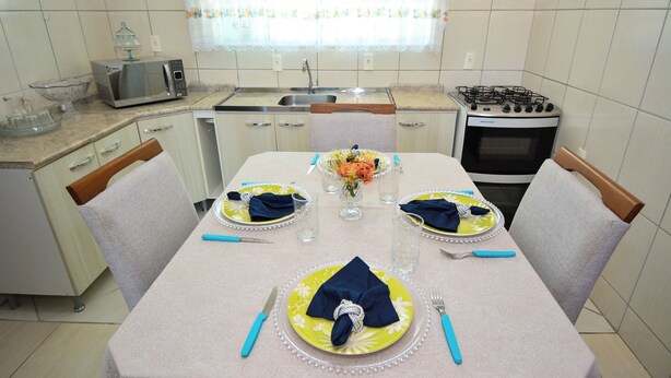 A kitchen with a dining table set for four, equipped with a microwave, stove, and sink. - Casa com Piscina a 250m da Praia PLH006 (Palhoça)