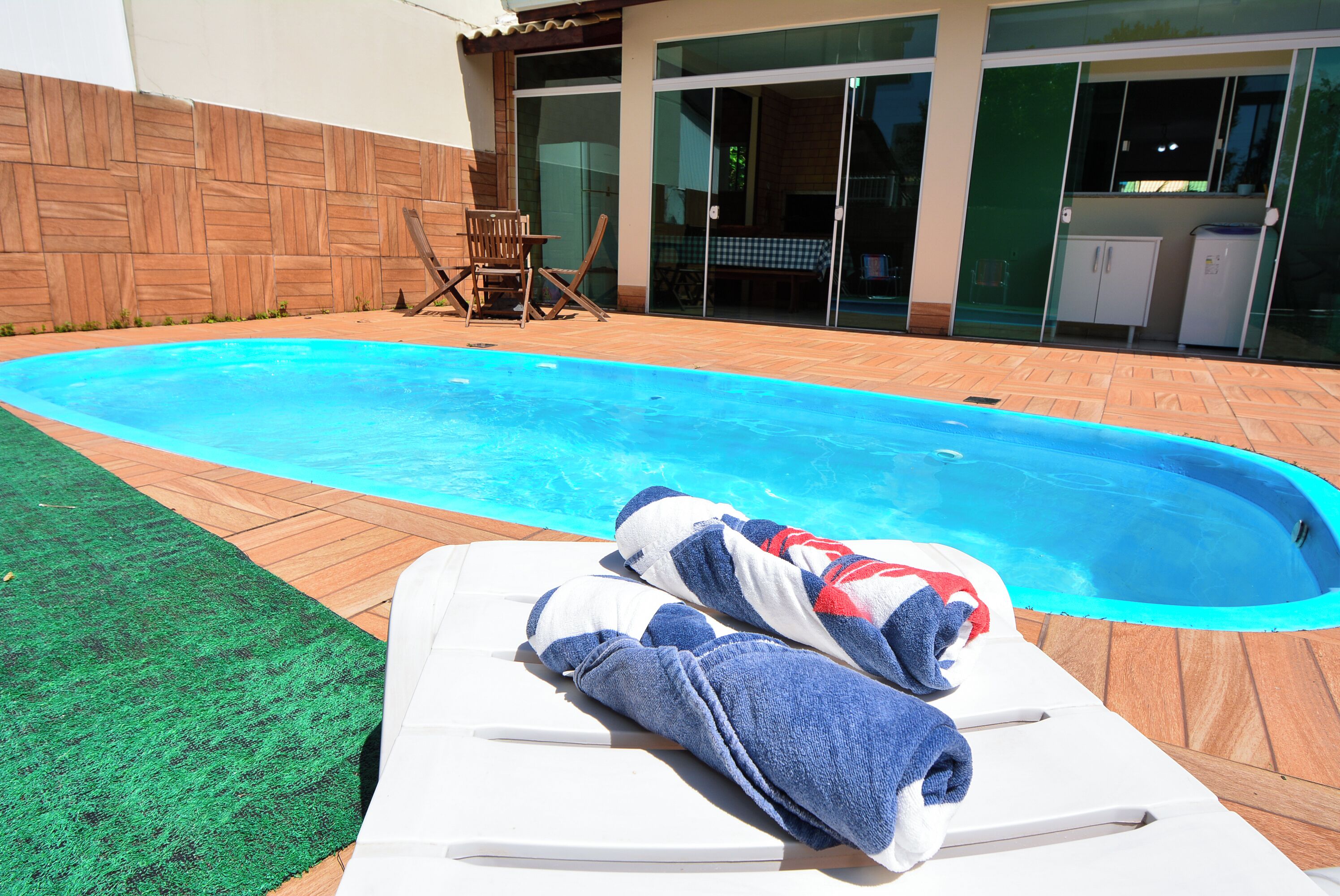 A swimming pool with lounge chairs and towels, a wooden deck, and a building with glass doors and windows.