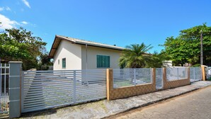 A residential building with a white exterior, a tiled roof, and a gated entrance with a white fence. - Casa com Piscina a 250m da Praia PLH006 (Palhoça)