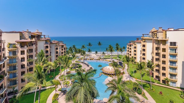Un resort con piscina central, palmeras y vistas al océano.