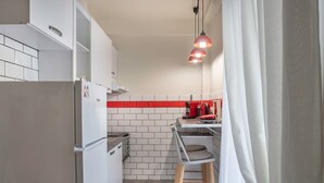 A compact kitchen with white cabinets, a red backsplash, and a single red hanging light. - The Athenian Penthouse Studio - An Urban Haven (Athens)