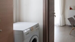 A laundry room with a washing machine, a wooden wardrobe, and a door leading to a bathroom with a shower and a chair. - The Athenian Penthouse Studio - An Urban Haven (Athens)