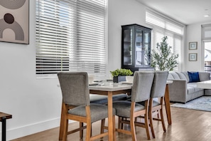 Un coin repas comprenant une table en bois, quatre chaises grises à revêtement, un buffet noir et un canapé gris.