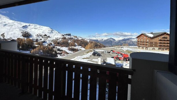 Une vue depuis un balcon donnant sur un paysage montagneux enneigé, avec des bâtiments et un véhicule rouge.