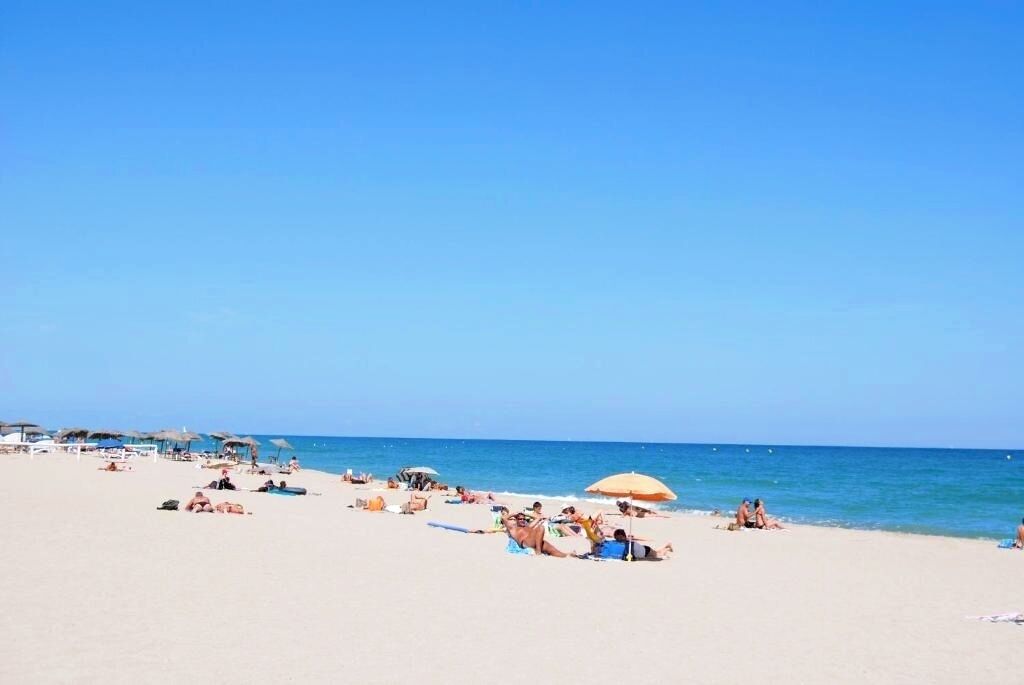 A beach with people sunbathing and swimming, umbrellas, and beach chairs.