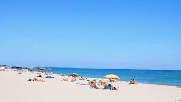 A beach with people sunbathing and swimming, umbrellas, and beach chairs.