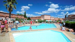 A swimming pool area with a clear blue sky, palm trees, and buildings with red-tiled roofs. - Air-conditioned house for 6 with supervised swimming pool, Walking distance to beach and port, Terrace (Saint-Cyprien)