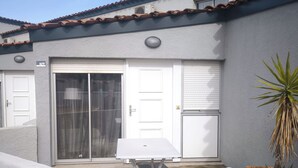 A residential building with a white exterior, a balcony with a white railing, a white table, and a potted plant. - Air-conditioned house for 6 with supervised swimming pool, Walking distance to beach and port, Terrace (Saint-Cyprien)
