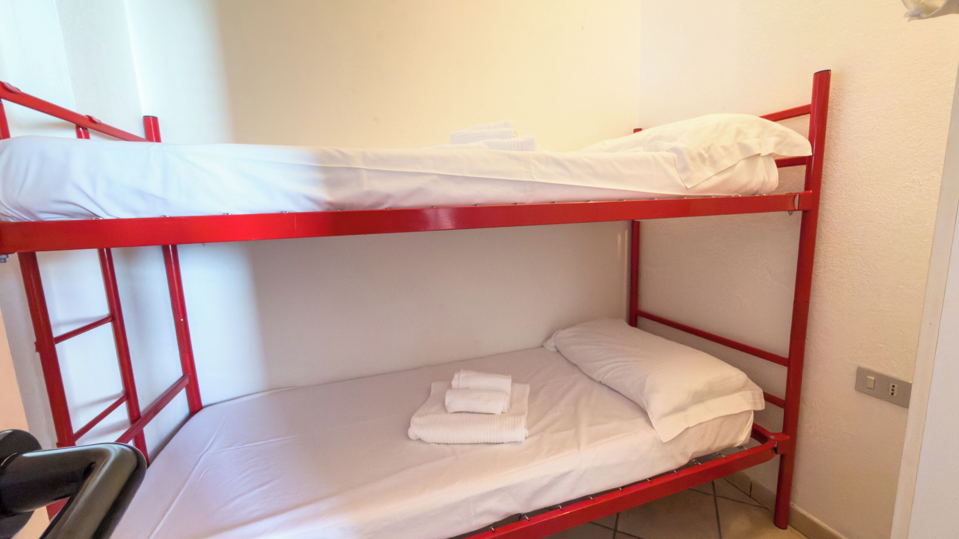 A bunk bed with white bedding and red metal frame.