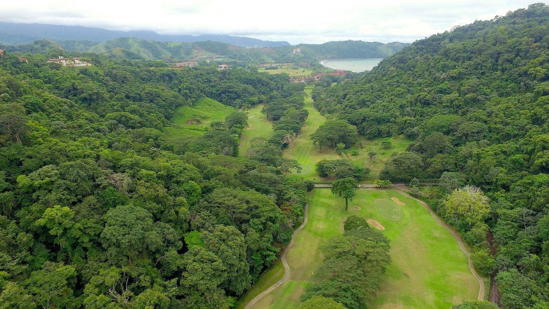 An aerial view of a lush green landscape with a golf course, surrounded by dense forest and hills.