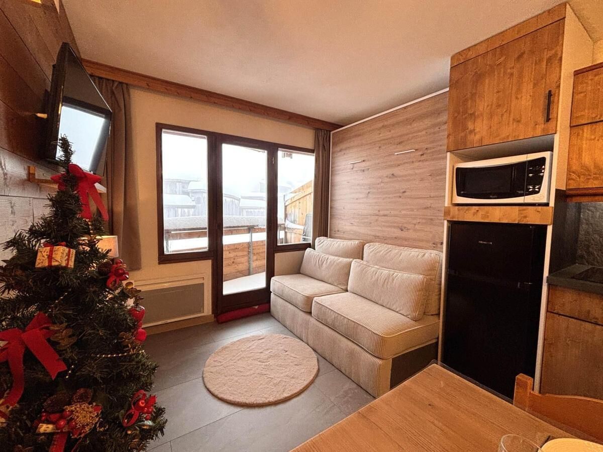 A cozy living room with a sofa, a small round rug, a Christmas tree, and a kitchen area with a microwave and refrigerator.