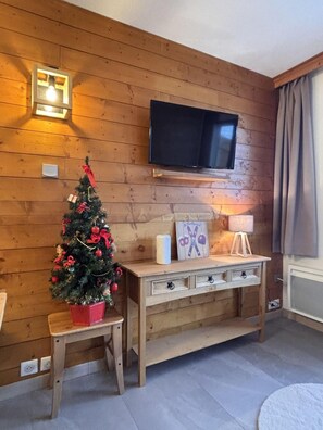Ein Zimmer mit Holzwänden, an der Wand befestigtem Fernseher, einem kleinen Weihnachtsbaum und einem Holzkonsole mit Schubladen.