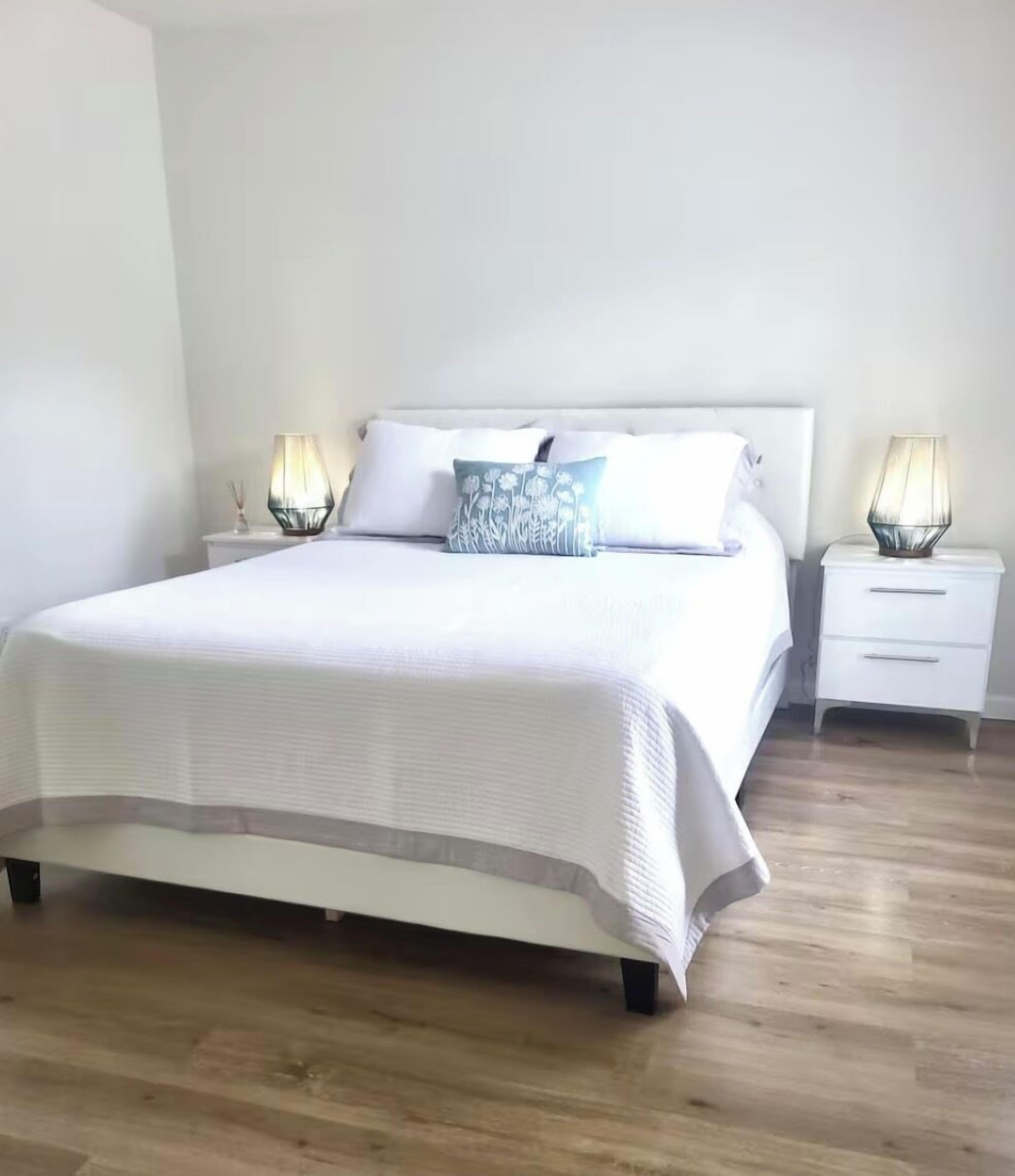 A neatly made bed with a white bedspread and two pillows, flanked by bedside tables with lamps.