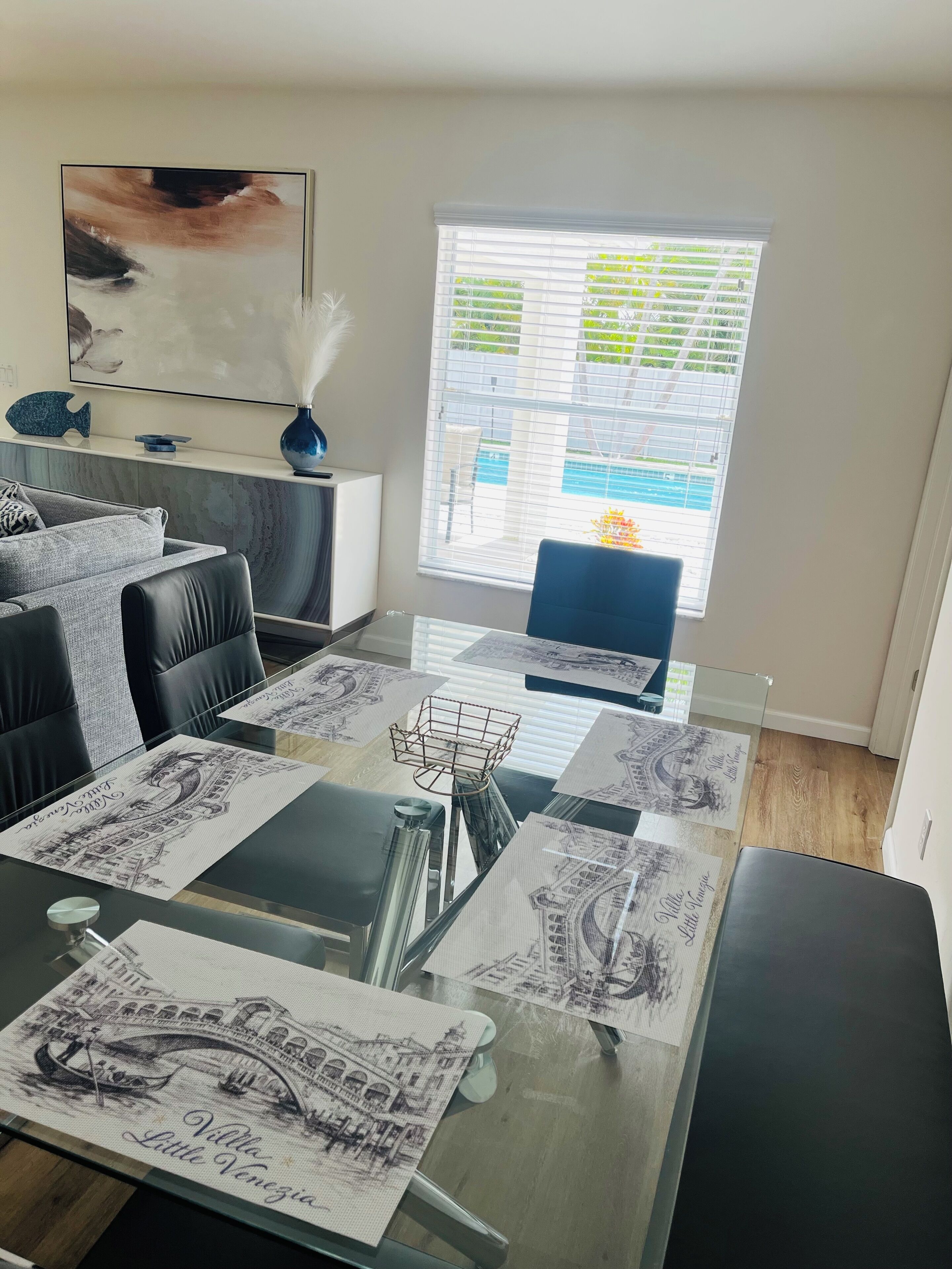 Un salón moderno con una mesa de centro de vidrio, un sofá y vistas a una piscina a través de una ventana.
