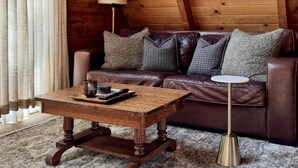 Ein Zimmer mit Holzwandverkleidung, einer Ledersofa, einem Holztisch und einer Lampe.